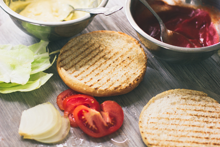 Top view on tow fresh tomatoes, burger's bun and sliced onion on wooden table as backgroundの写真素材