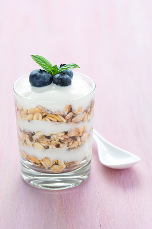A glass of layered yoghurt, cereals, blueberry and mint on a pink background.の写真素材