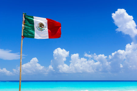 Mexican national flag flying in the wind on an amazing sandy beach in front of turquoise water of the caribbean sea, near Cancun, Mexicoの写真素材