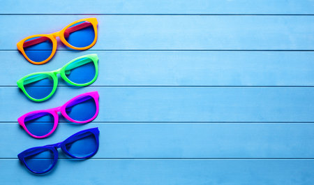Collection of colorful sunglasses on blue wooden background.