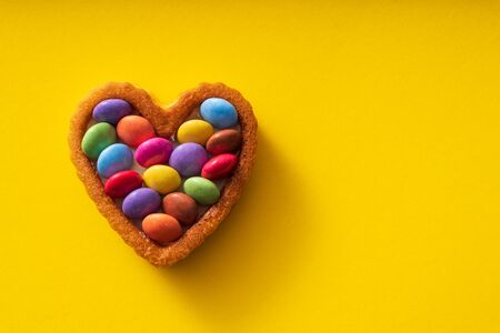 Colorful Candy Buttons on Heart shaped cake on yellow Background - Birthday conceptの写真素材