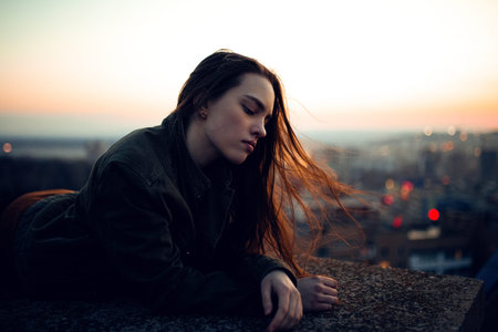 The girl in the jacket lies on the roof against the backdrop of the sunsetの写真素材