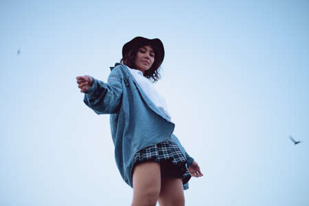A girl in a hat and a denim jacket walks on the roof at sunsetの写真素材