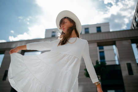 Portrait of a girl with glasses in a white dress and a white hat during a strong wind in a Park in Ufaの写真素材