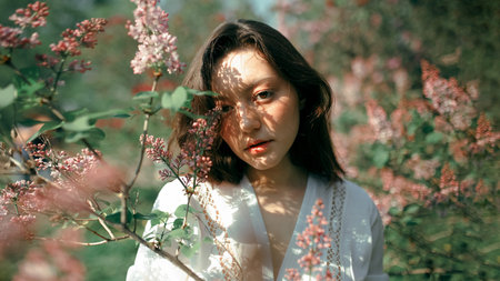 A girl in a light white semi-transparent dress walks through a summer flower gardenの写真素材