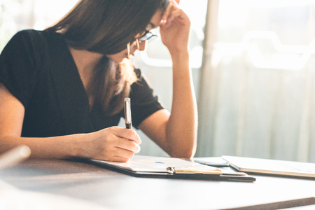 Photo business woman wearing suit, looking smartphone and holding documents in hands. Open space loft office,young business woman reading sitting at the desk on office backgroundの写真素材