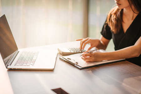 Photo business woman wearing suit, looking smartphone and holding documents in hands. Open space loft office,young business woman reading sitting at the desk on office backgroundの写真素材