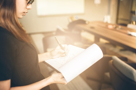 Photo business woman wearing suit, looking smartphone and holding documents in hands. Open space loft office,young business woman reading sitting at the desk on office backgroundの写真素材