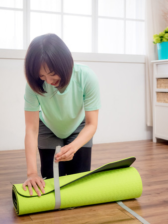 Young woman folding green yoga or fitness matの写真素材