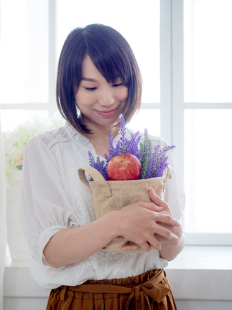 A young asian woman holding a bouquet of fresh flowers by the windowの写真素材