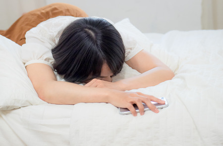 Young woman tired and sleeping with cellphoneの写真素材