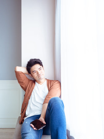 Young man wearing casual clothes and holding phone ,resting by the window