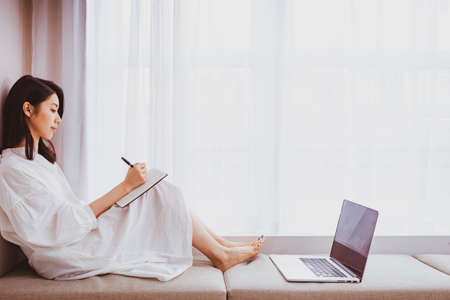 A beautiful Asian women writes something in a bookの写真素材