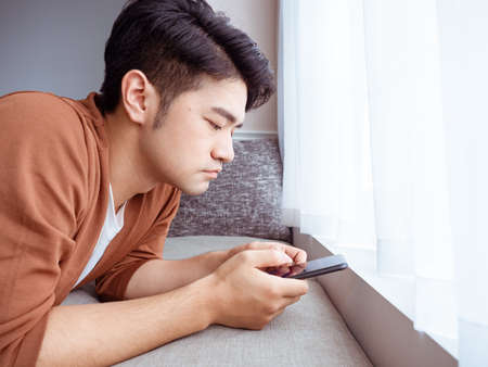 Young man wearing casual clothes and using smartphone at homeの写真素材