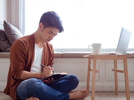 Young Asian man writing in a bookの写真素材