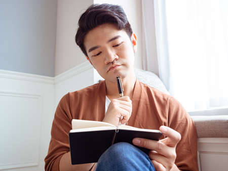 Young Asian man writing in a bookの写真素材
