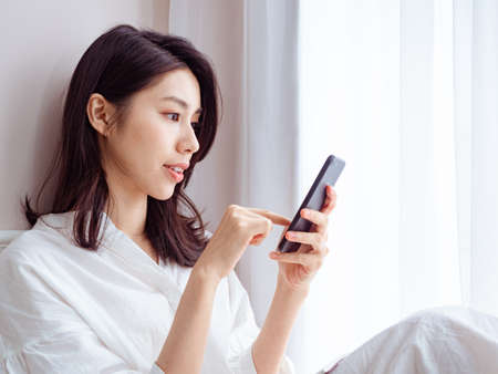 Young asian woman using smartphone at homeの写真素材