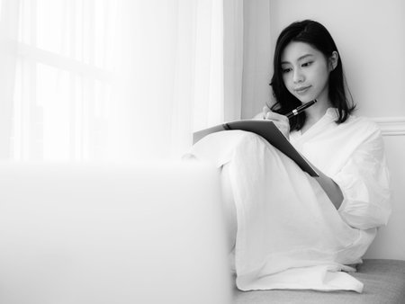 A beautiful Asian women writes something in a book in black and whiteの写真素材