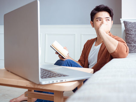 Young asian man reading a book while relaxing at home