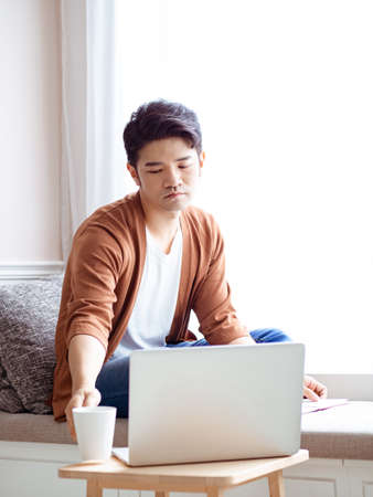 Asian young man sitting at the table in front of laptop computerの写真素材