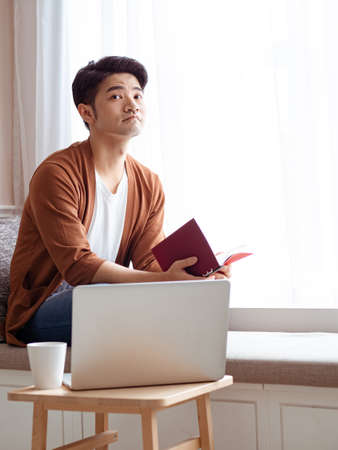 Asian young man sitting at the table in front of laptop computerの写真素材