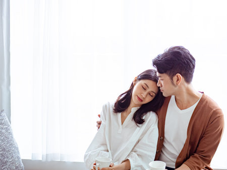 Young asian woman and man at home with cup of coffee in hands.