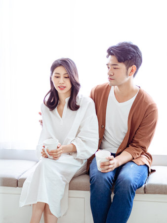 Young asian woman and man at home with cup of coffee in hands.の写真素材