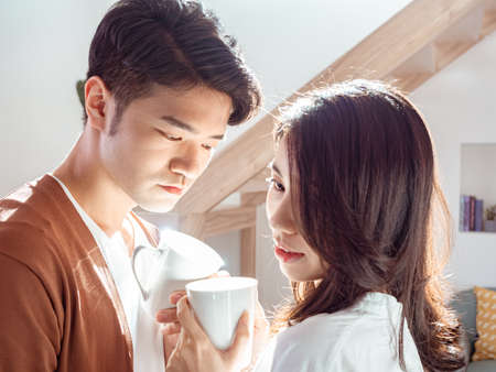 Young asian woman and man are enjoying spending time together at home with cup of coffee in hands.の写真素材
