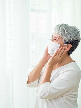 Asian senior woman wearing facemask during  flu outbreak. Virus and illness protection, home quarantine.の写真素材