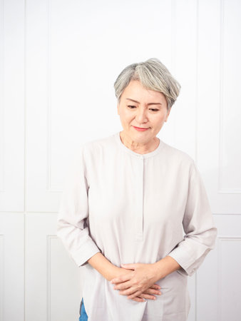 Senior asian woman wearing casual clothes with hand on stomach because indigestion, painful illness feeling unwell. ache concept.の写真素材