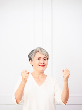 Senior beautiful asian woman wearing casual dress standing and raising fists.の写真素材