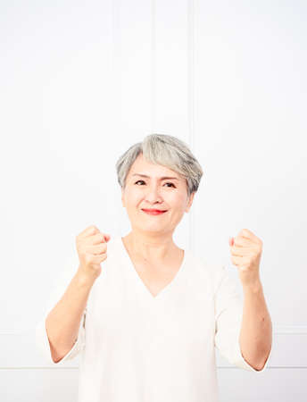 Senior beautiful asian woman wearing casual dress standing and raising fists.の写真素材
