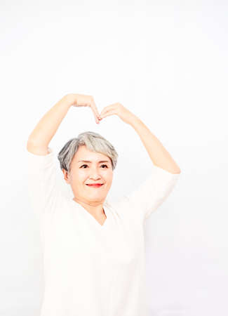 Senior beautiful grey-haired woman wearing casual shirt smiling in love doing heart symbol shape with hands in white background.の写真素材