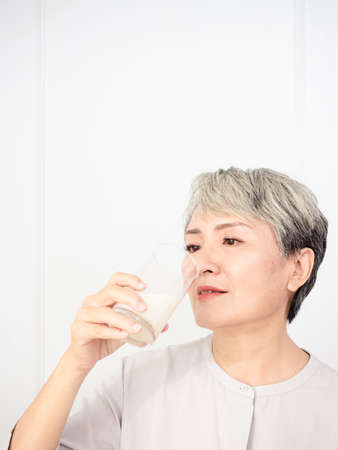 Portrait of a senior asian woman with a glass of milk.の写真素材