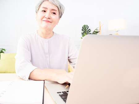 Senior asian woman sitting at the table at home working using  laptop.の写真素材