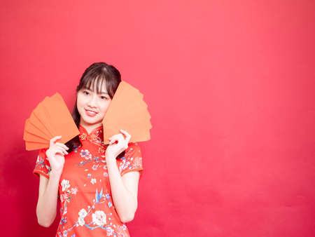 Portrait beautiful young asian woman wearing traditional cheongsam qipao dress with red envelopes in chinese new year concept on red background.の写真素材