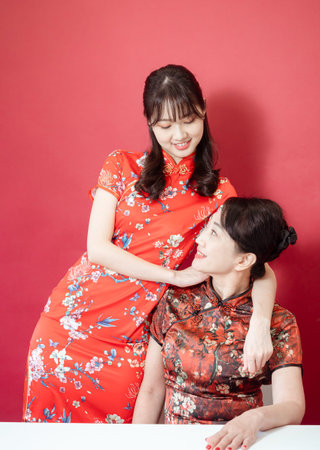 Mature asian mother hugging with her asian daughter on red background(Both wearing traditional cheongsam qipao).の写真素材