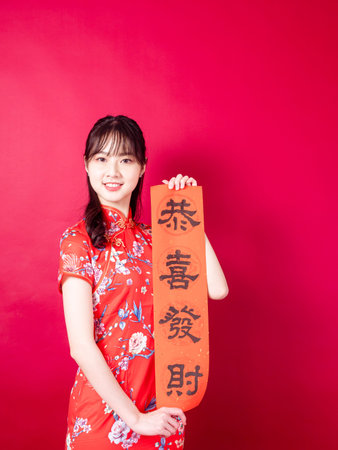 Young asian woman wearing traditional cheongsam qipao dress hold Chinese festival couplet to...
