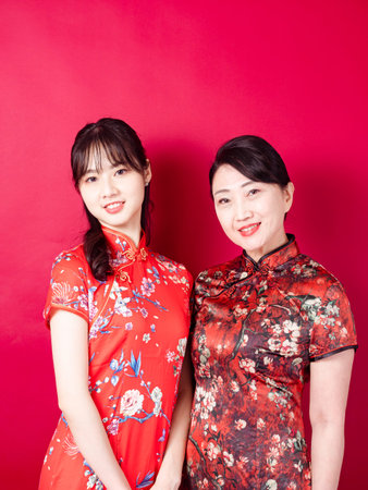 Portrait of a daughter and mother wearing traditional cheongsam qipao isolated on red background.の写真素材