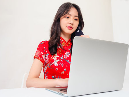 Asian young woman wearing traditional cheongsam qipao dress using laptop and credit card shopping online, e-commerce concept isolated on white background.の写真素材