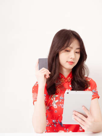Asian young woman wearing traditional cheongsam qipao dress using digital tablet and credit card shopping online, e-commerce concept isolated on white background.の写真素材