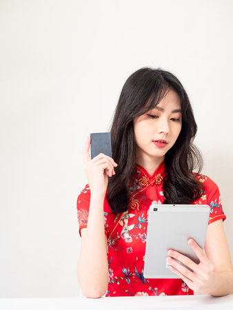 Asian young woman wearing traditional cheongsam qipao dress using digital tablet and credit card shopping online, e-commerce concept isolated on white background.の写真素材
