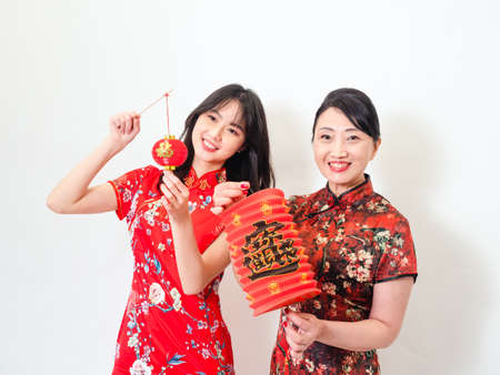 Portrait of young asian woman and elder woman both wearing traditional cheongsam qipao dress hold red paper lantern with word meaning good fortune and treasure on white background.の写真素材
