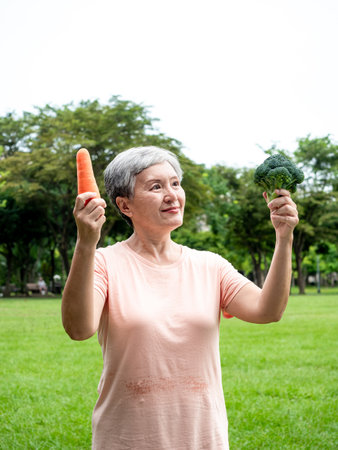 Portrait of happy senior adult elderly asia woman smiling standing and holding fresh vegetable in the park.の写真素材