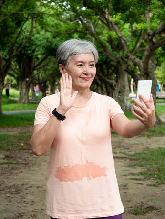 Portrait of senior adult elderly asian woman 60s smiling standing and holding smartphone in the...