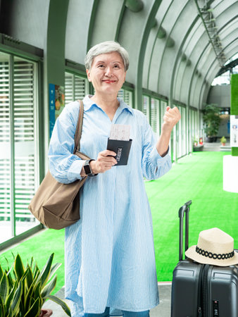 Portrait of senior adult elderly asian woman 60s smiling standing with suitcase luggage bag and holding passport with ticket for travel concept.の写真素材