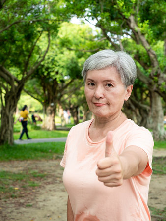 Portrait of happy senior adult elderly asia woman 60s showing big thumbs up in the park.の写真素材