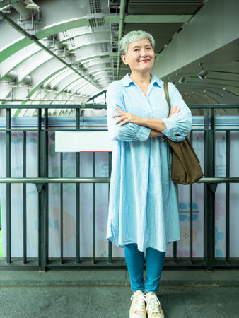 Portrait of senior adult elderly asian woman 60s smiling standing and crossing arms on chest interior in public.の写真素材
