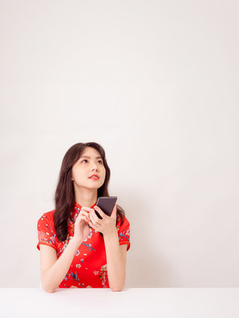 Smiling young asian woman in traditional cheongsam qipao dress using a smart phone isolated on white background.の写真素材