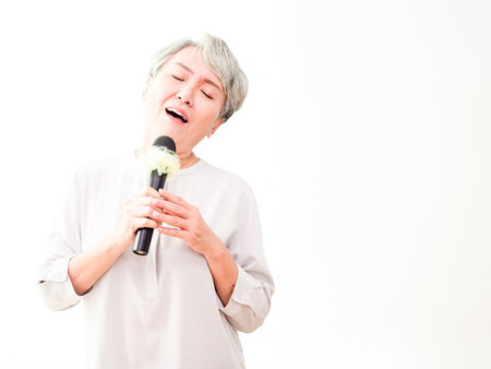 Happy senior asian woman singing with microphone on white background.の写真素材